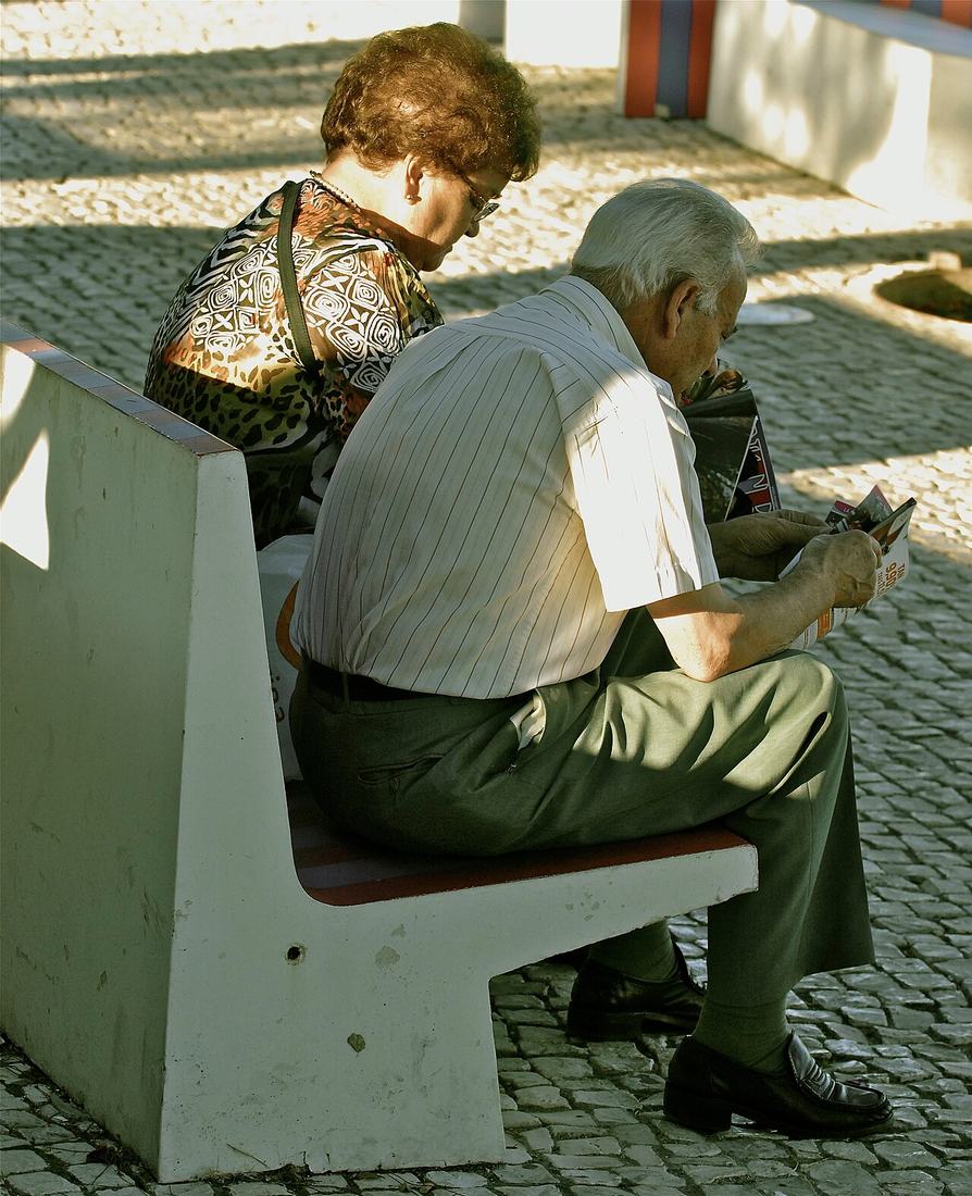 Casal de idosos lendo juntos em um banco
