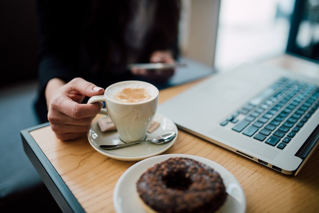 Mulher usando o celular com café e laptop sobre a mesa
